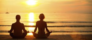 Young couple practicing yoga on the beach at sunset.